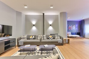 A modern living room with a grey sofa, two armchairs, a coffee table, and a flat-screen TV.
