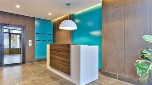 Un área de recepción con un mostrador de madera, una pared de acento color aguamarina y una lámpara colgante moderna.