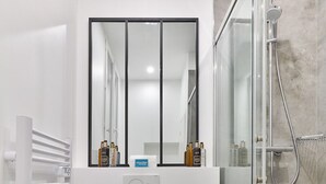 Une salle de bain moderne équipée de toilettes, d’une douche à parois de verre, d’un porte-serviettes et d’un miroir.