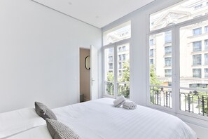 A bedroom with a large window, a bed, and a door leading to another room.