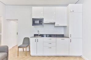 A modern kitchen with white cabinets, a built-in microwave, and a grey chair.