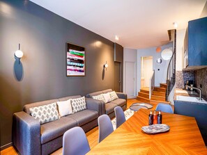 A modern living room with a sofa set, a dining table, and a kitchen area with a staircase.