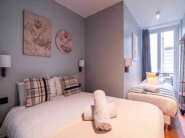 A hotel room with two beds, a large window, and artwork on the walls.