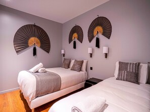 Habitación de hotel con dos camas, un ventilador de pared y una mesita de noche.