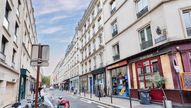 A street view with buildings, a parked motorcycle, and a closed shop with a red awning. - UrbanFlat 136 - Large Apartment in Paris Center (Paris)