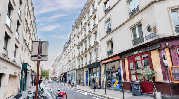 Vista de la calle con edificios, una motocicleta estacionada y una tienda cerrada con toldo rojo.