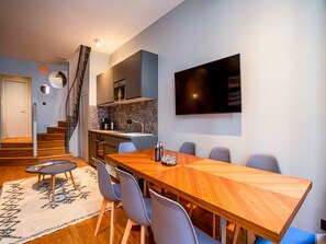 Una cocina moderna con horno integrado, un comedor con mesa y sillas de madera, y una escalera que sube a otro nivel.