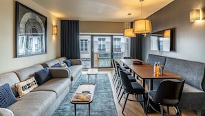 Ein modernes Hotelzimmer mit einer Couch, einem Esstisch und Stühlen, einem großen Fenster mit Ausblick und einem Wandbild.