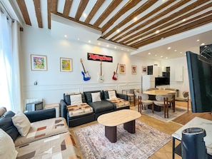 A living room with a sofa, coffee table, and a dining area with chairs. - UrbanFlat 68 - Cosy Rolling Stones Apartment Paris (París)