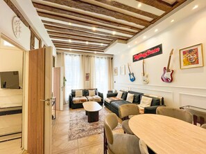 Een woonkamer met een bank, een salontafel, een eettafel met stoelen, en een zichtbare keuken door een open deur.