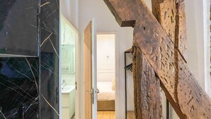 A hallway with a wooden beam, a bathroom with a white sink, and a door leading to a bedroom.