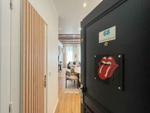 A hallway leading to a room with a Rolling Stones logo, a number 68 sign, and a view into a living area with a TV and seating. - UrbanFlat 68 - Cosy Rolling Stones Apartment Paris (París)