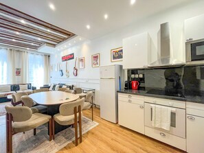 A modern kitchen with white cabinets, a dining table with chairs, and a coffee maker. - UrbanFlat 68 - Cosy Rolling Stones Apartment Paris (París)