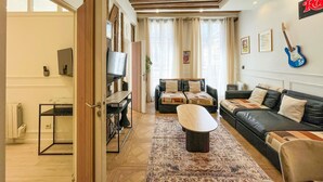 A living room with a sofa, a coffee table, a TV, and a guitar on the wall.