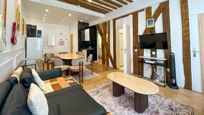 A modern living room with a sofa, a coffee table, and a TV. There is a kitchen area with a refrigerator and a microwave.