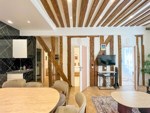 Una sala de estar moderna con techo de madera, televisor, comedor y cocina con baldosas negras.