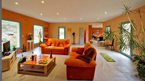 Un salon spacieux avec des canapés orange, une table basse en bois et de grandes fenêtres.