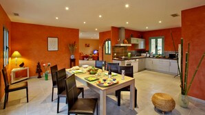 Une cuisine moderne avec un coin repas, comprenant une grande table dressée pour un repas, un téléviseur en arrière-plan et un plan de travail équipé d’appareils électroménagers.