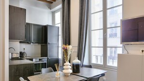 A modern kitchen with dark cabinets, a built-in oven, and a dining area with a marble table and chairs.