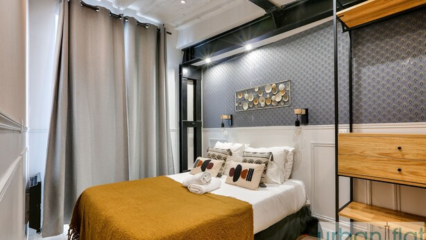 A modern bedroom with a bed, a wooden nightstand, a wall-mounted shelf, and a patterned wallpaper.