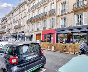 A street with parked cars, a building with a red awning, and a shop with a sign. - Urban Flat 62 - Charming 3BDR Apartment near Champs-Elysees (París)