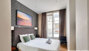 Una camera d'albergo con un letto grande, un quadro, una finestra con tende e una poltrona.