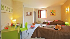 Een hotelkamer met een bureau, twee bedden, een stoel, een raam en kunstwerken aan de muren.