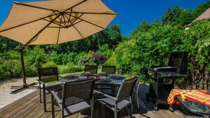 Een terras buiten met een tafel, stoelen, een barbecue en een grote parasol.