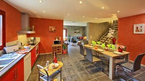 Een moderne keuken met rode kastjes, een eethoek met een houten tafel en stoelen, en een trap naar een hoger niveau.