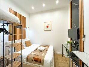 Een hotelkamer met een bed, een televisie, een bureau en een wandplank.