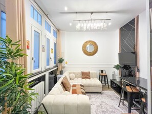 Een moderne woonkamer met een hoekbank, een eethoek met een zwarte tafel en een grote flatscreen televisie aan de muur.
