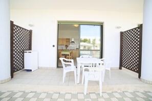 An outdoor patio area with a table and chairs, a sliding glass door leading to a kitchen, and a white wall with a wooden lattice design. - Cala Verde Residence - Two-room apartment for 4 people (Marina di Mancaversa)