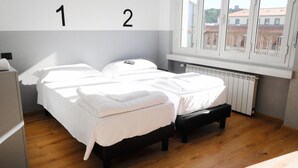 A bedroom with two beds, a radiator, and a window with a view of buildings. - Hotello Hostel (Trieste)