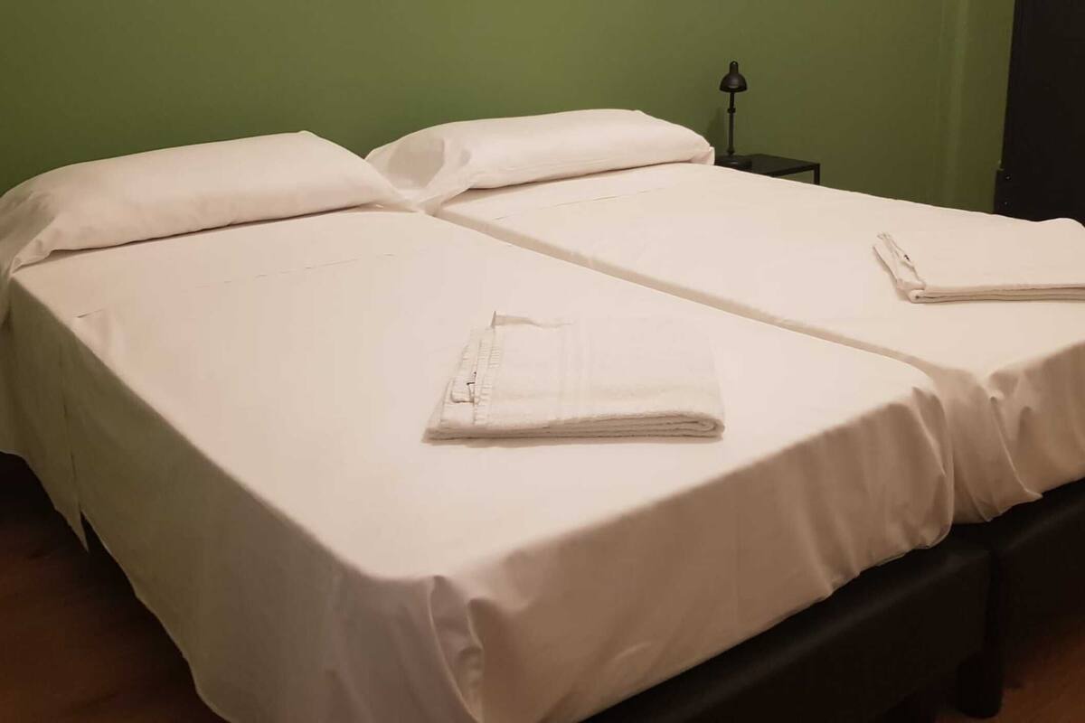 Un lit double avec du linge de lit blanc et deux serviettes pliées sur chaque lit.