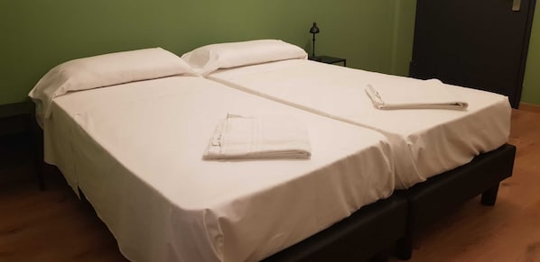 Una cama doble con sábanas blancas y dos toallas dobladas sobre cada cama.