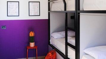 A bunk bed room with a purple wall, a small stool with pencils, and a red backpack on the floor.