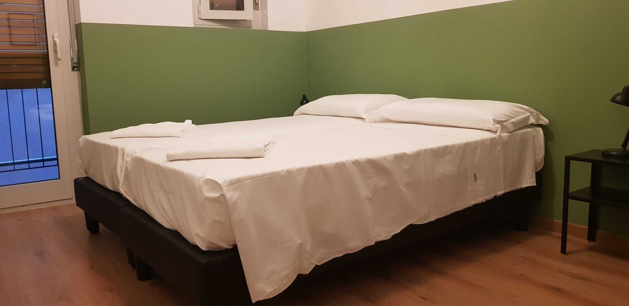 A single bed with white bedding in a room with green walls and a wooden floor.