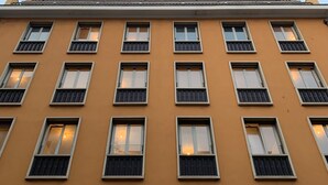 A multi-story building with a yellow facade, multiple windows with metal grilles, and a visible balcony railing. - Hotello Hostel (Trieste)