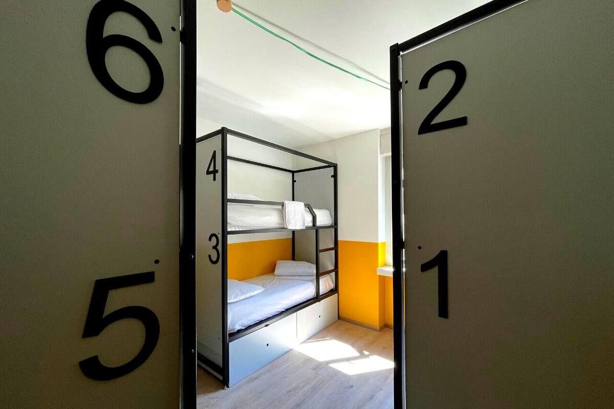 Une chambre de dortoir avec des lits superposés, des portes numérotées et une fenêtre laissant entrer la lumière naturelle.