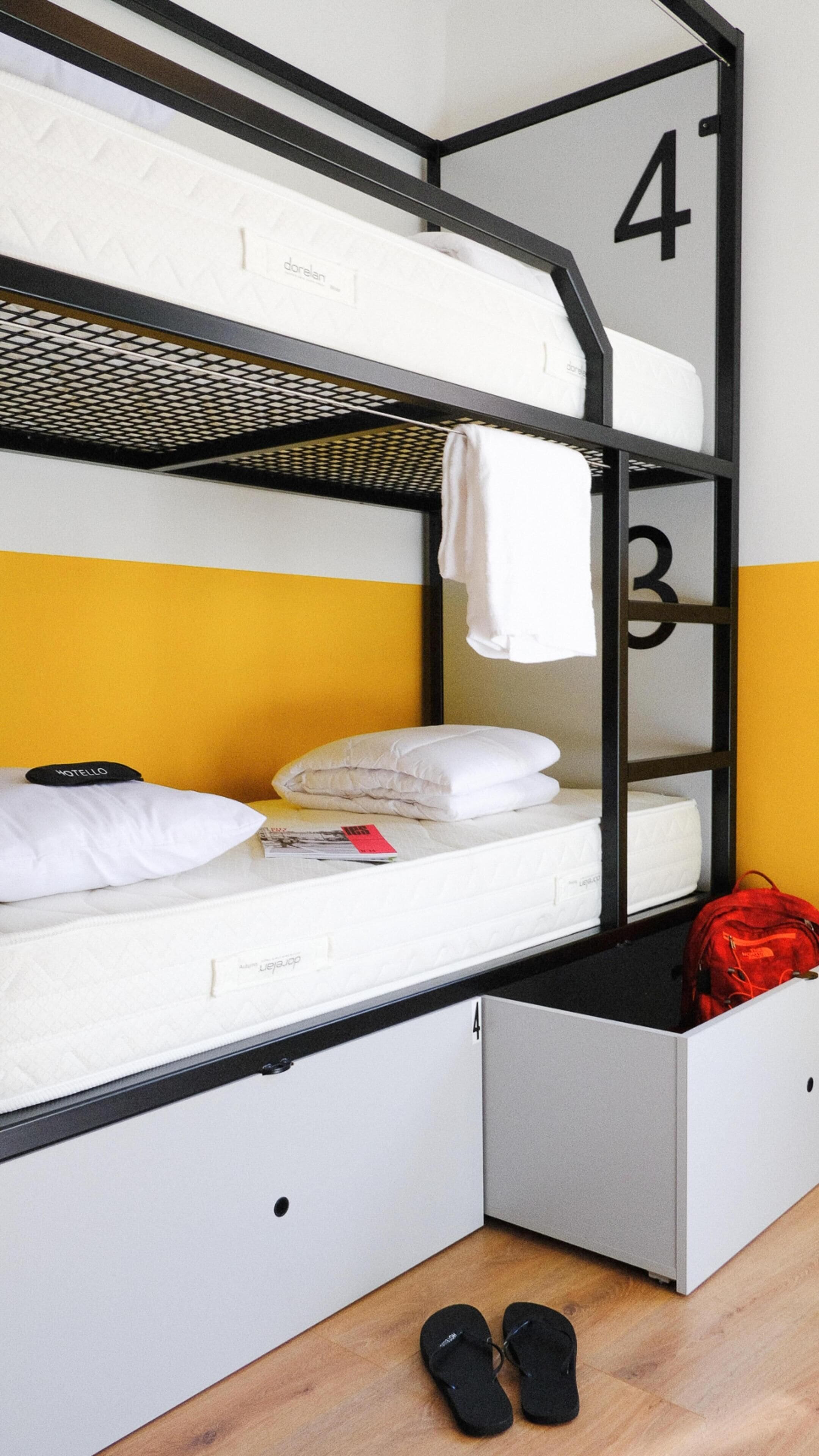 A bunk bed with a mattress labeled "Dormezap" and a red backpack on the lower bunk.