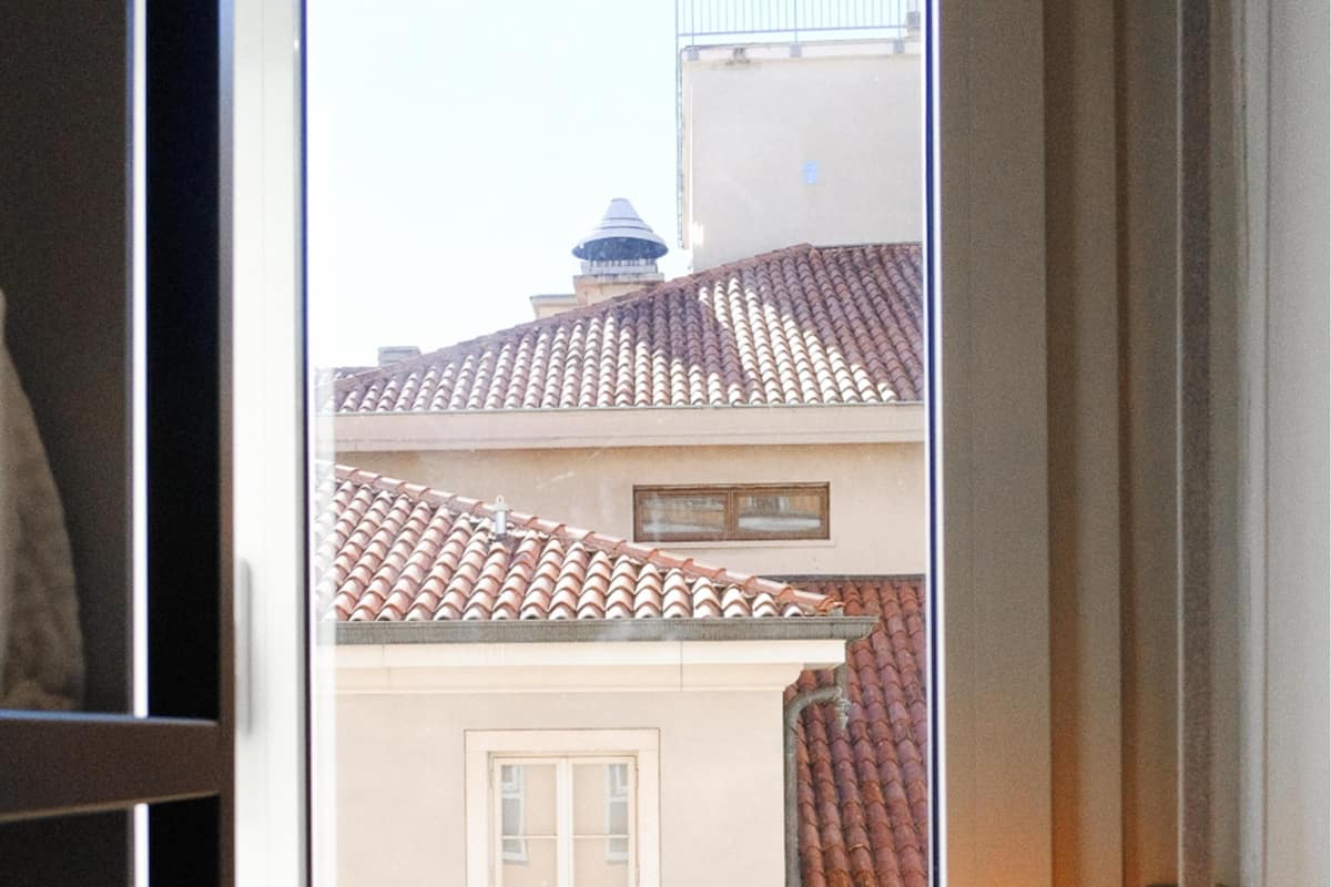 Une vue à travers la fenêtre d’un bâtiment doté d’un toit recouvert de tuiles et d’une petite fenêtre.