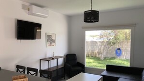 A modern living room with a flat-screen TV, a coffee table, a sofa, and a dining area with chairs and a small table. - Rocamar House (Barbate)