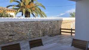 An outdoor patio with stone walls, wooden benches, and a view of palm trees. - Rocamar House (Barbate)