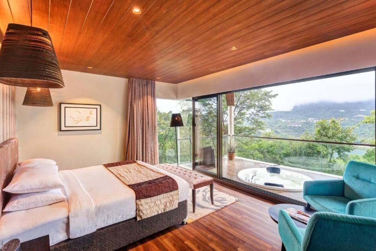A modern bedroom with a large bed, a view of the outdoors, and a balcony with a hot tub.