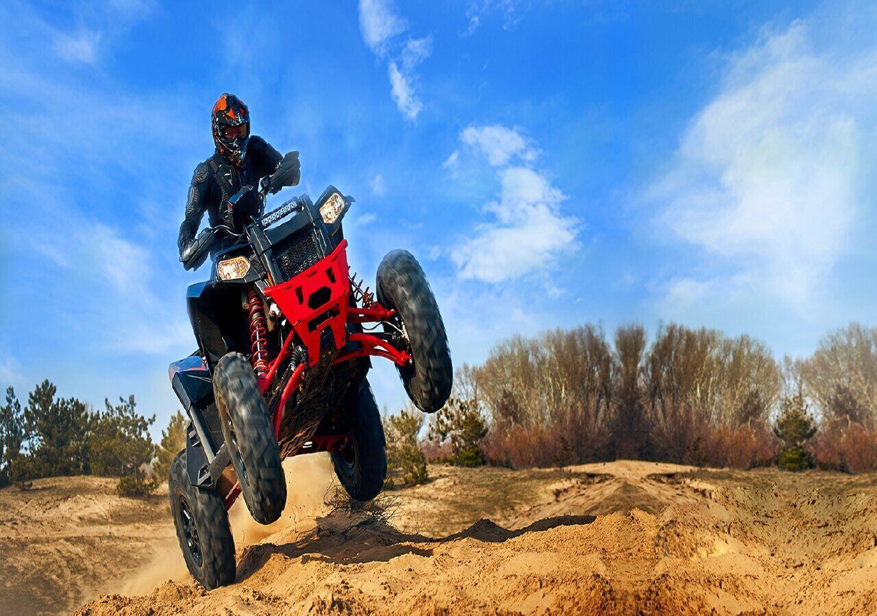 A person riding a red ATV on a dirt path with trees in the background.