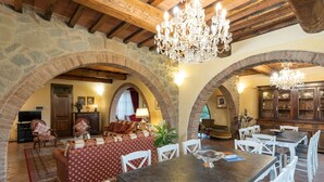 Un comedor espacioso con una mesa grande y sillas blancas, rodeado de arcos de piedra y vigas de madera.