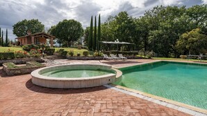 Una piscina con hidromasaje circular, sillas de descanso y una pérgola con sombrillas.