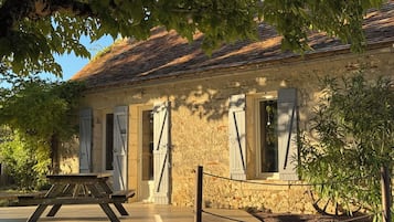 Un bâtiment rustique en pierre, avec un toit en tuiles, des volets en bois et une table de pique-nique à l’extérieur.