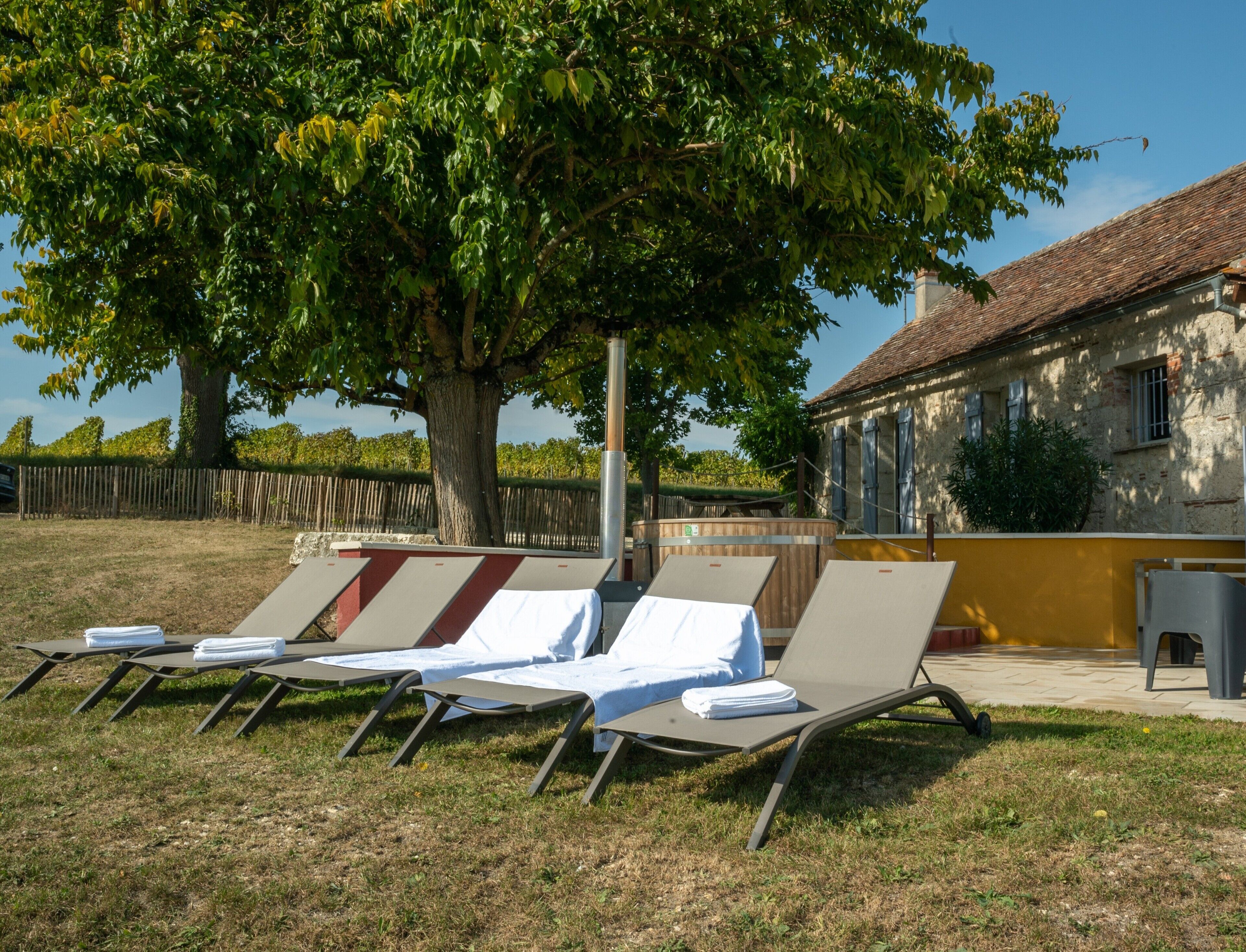 Une rangée de chaises longues avec des serviettes blanches, un arbre et un bâtiment avec un toit en tuiles.