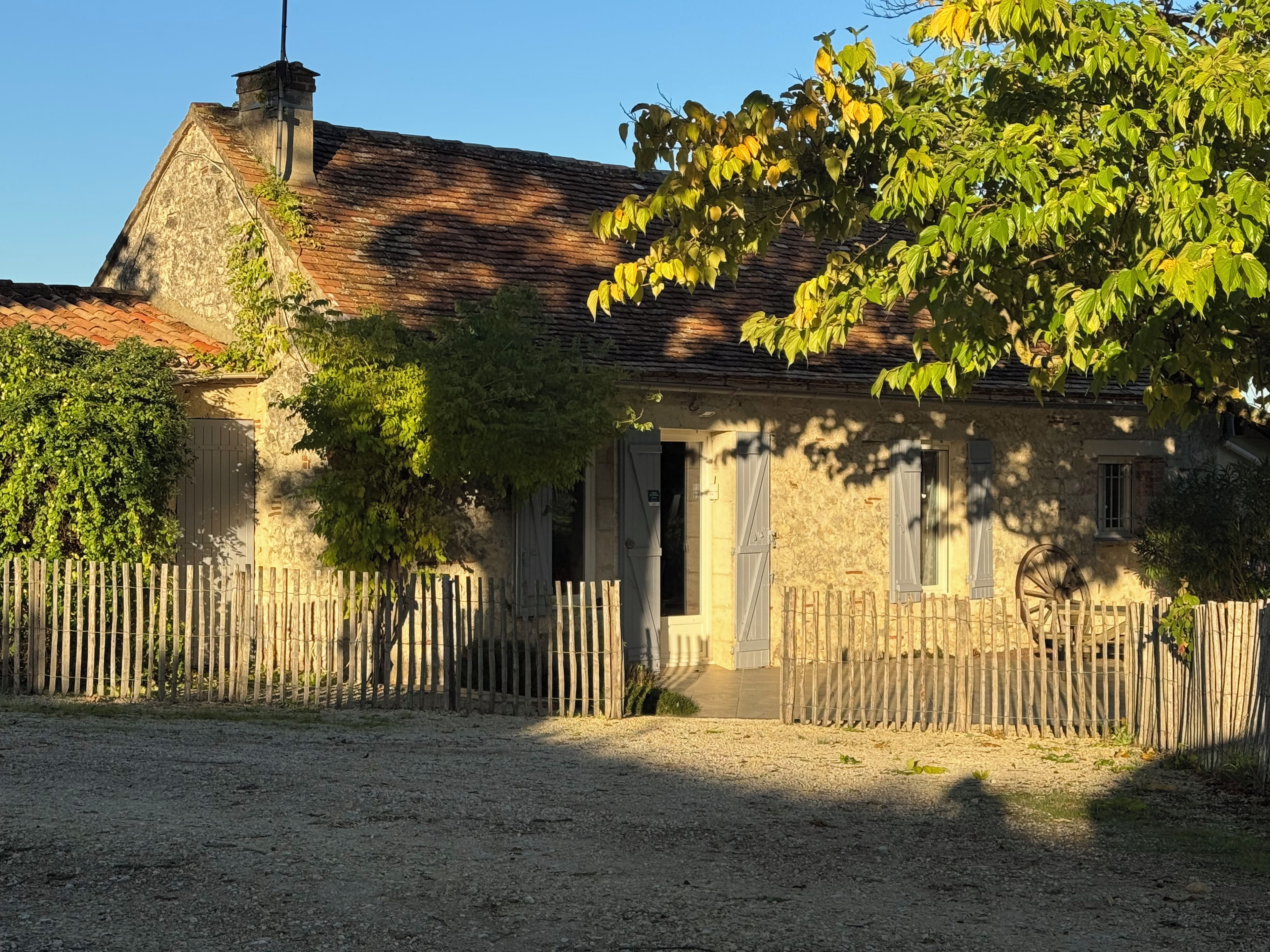 A rustic stone building with a wooden fence, a chimney, and a tree in the foreground.